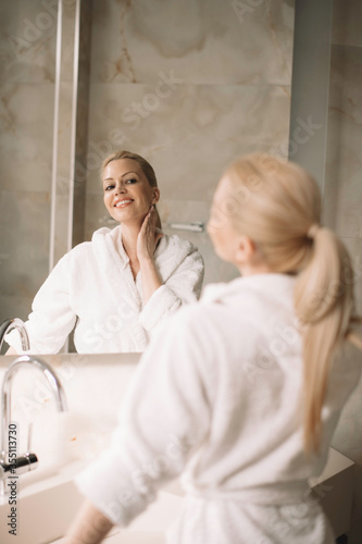 Beautiful woman enjoying in hotel. Young happy woman in bathrobe use the cream for the body.