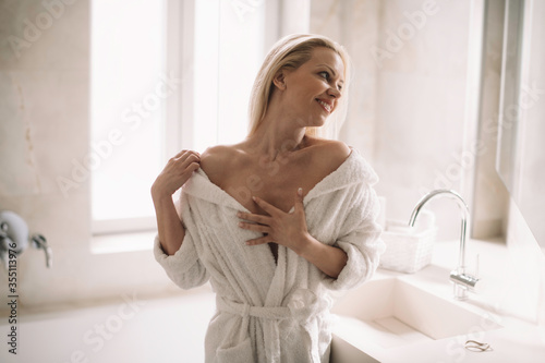 Beautiful woman enjoying in hotel. Young happy woman in bathrobe use the cream for the body.