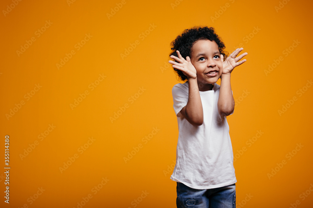 African American boy in a white T-shirt holds his hands near his face ...