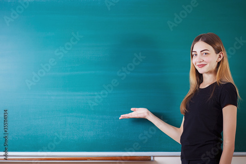 Beautiful sudent girl shows on empty copy space on the school board. Education concept. photo