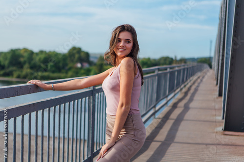 Pretty young woman posing on the old rusty transport bridge over the river during sunset.