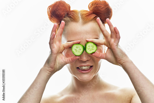 a close-up portrait of a red-haired girl with a green cucumber in her hands and next to her face. Isolated on a white background.