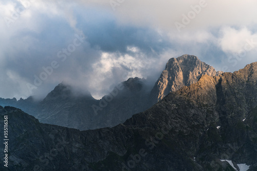 Dark cloudy sunset with light catching a little piece of rock. Dangerous conditions in Tatra Mountains with huge part covered with black shadow before heavy storm.