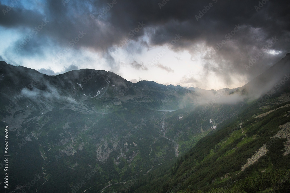 Dark cloudy sunset with light catching a little piece of rock. Dangerous conditions in Tatra Mountains with huge part covered with black shadow before heavy storm.