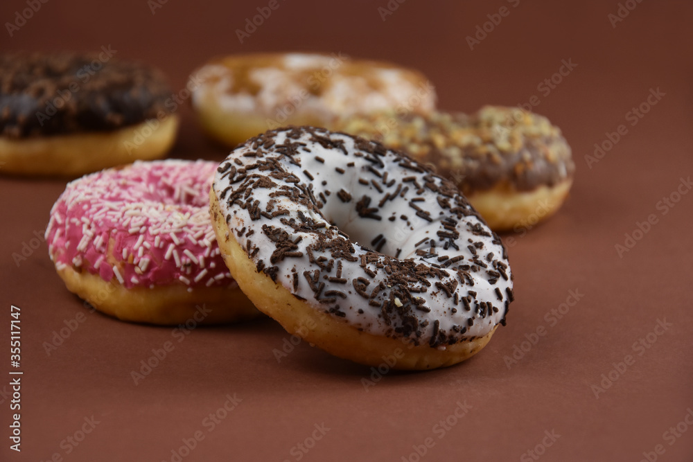 Detail on white donut with chocolate sprinkles stock images. Different donuts on a brown background stock images. Pile of different glazed donuts images. American delicacy food