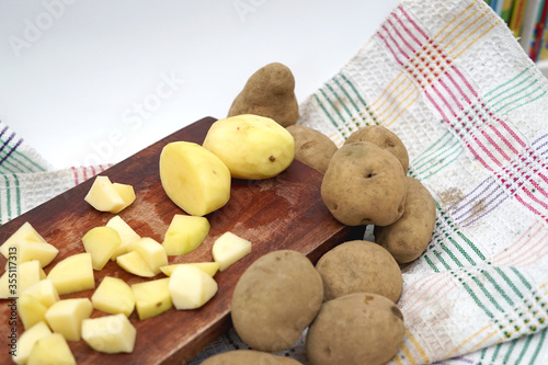 Pile of potato slice and unpeeled above wood cutting board