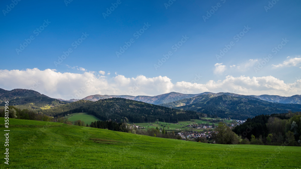 Germany, Green meadows and trees of black forest nature landscape with moving clouds and shadows over mountains and valleys at a small village