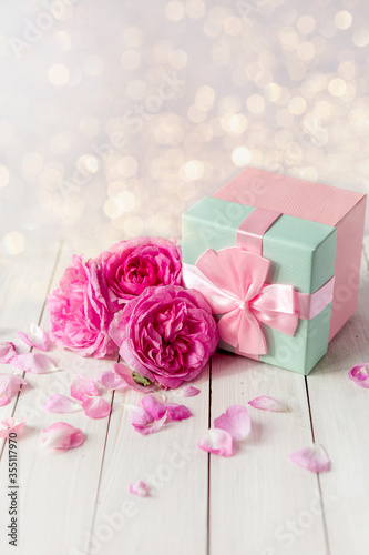 pink gift box surrounded by roses. gift box with bow ribbon on white table.Greeting card for Birthday, Womans or Mothers Day.