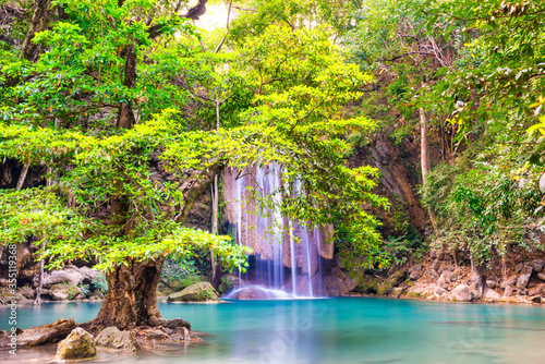 Beautiful waterfall in tropical jungle forest with big green tree and emerald lake on foreground. Nature landscape of Erawan National park  Kanchanaburi  Thailand