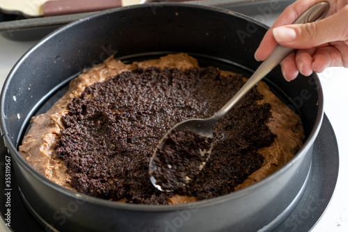 Making a cake in a baking dish. Chocolate dough and poppy seed filling. Woman smoothes the surface with a spoon