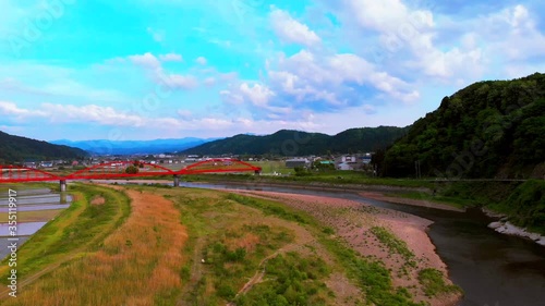 自然に恵まれた土地の河川にかかる赤い橋を空撮