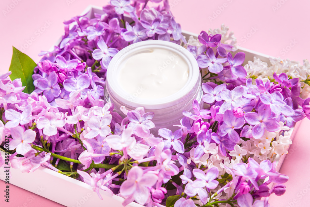 Jar of natural face cream with lilac flowers on pink background Jar of natural face cream with lilac flowers on pink background