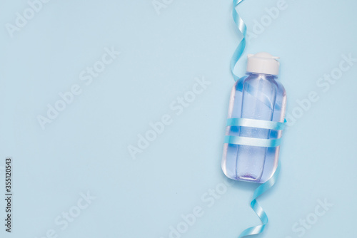 cosmetic bottle with tonic or micelar water with ribbon on blue background. flat lay photo