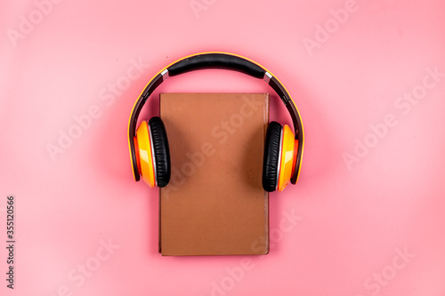Book and yellow headphones on. Pink background top view