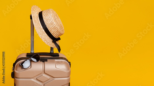 Summer Travel. Suitcase with sun glasses and hat over yellow background