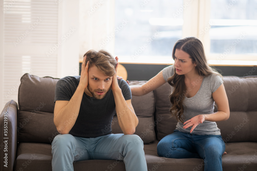 Long-haired young woman blaming her husband while he closing his ears Long-haired young woman blaming her husband while he closing his ears