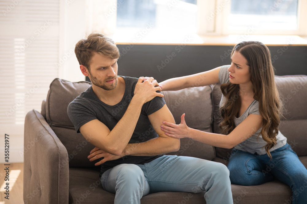 Obraz premium Long-haired young woman blaming her husband while he sitting with upset look