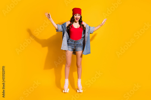 Omg i can ride. Full body of surprised youth student girl stay on roller blades impressed scream hold hands wear red headwear singlet denim isolated over bright color background