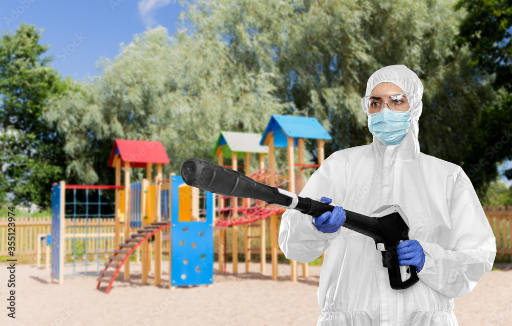 disinfection service and pandemic concept - sanitation worker in protective gear, medical mask, gloves and goggles with pressure washer or sanitizer over children's playground background disinfection service and pandemic concept - sanitation worker in protective gear, medical mask, gloves and goggles with pressure washer or sanitizer over children's playground background