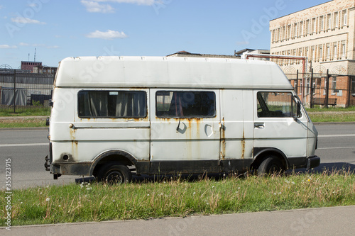 White rusty abandoned compact van. Unnecessary malfunctioning car junk truck abandoned on the side of the road in the industrial part of the city.
