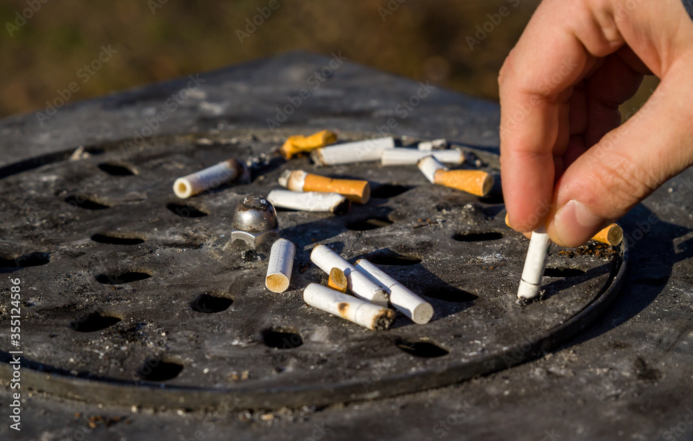 Close up picture of dirty street ashtray with a hand extinguishing