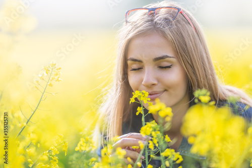 Beautiful young girl smells yellow flowers on a meadow with her eyes closed, smiling