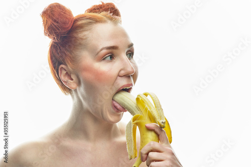 Red-haired girl with a banana in her hands. Holds a banana next to his face and lips. Isolated on a white background.