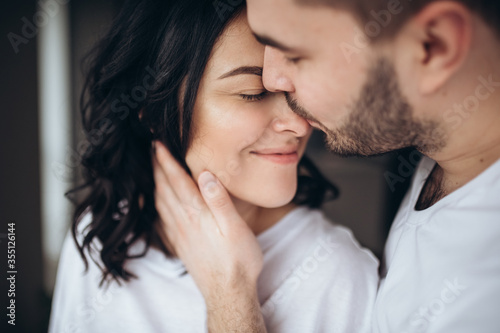 Stunning sensual intdoor portrait of young stylish fashion couple in love. Woman and man embrace and want to kiss each other. They are smiling and looking to each other