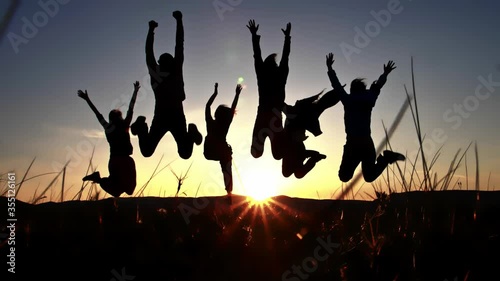 Silhouette of group friends that jumping together on the hilltop and raising hands to the sky photo