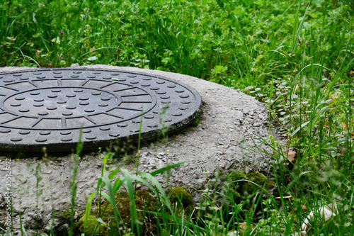 Manhole of a sewer or drain with a plastic round cover surrounded by green grass in the backyard of the house.