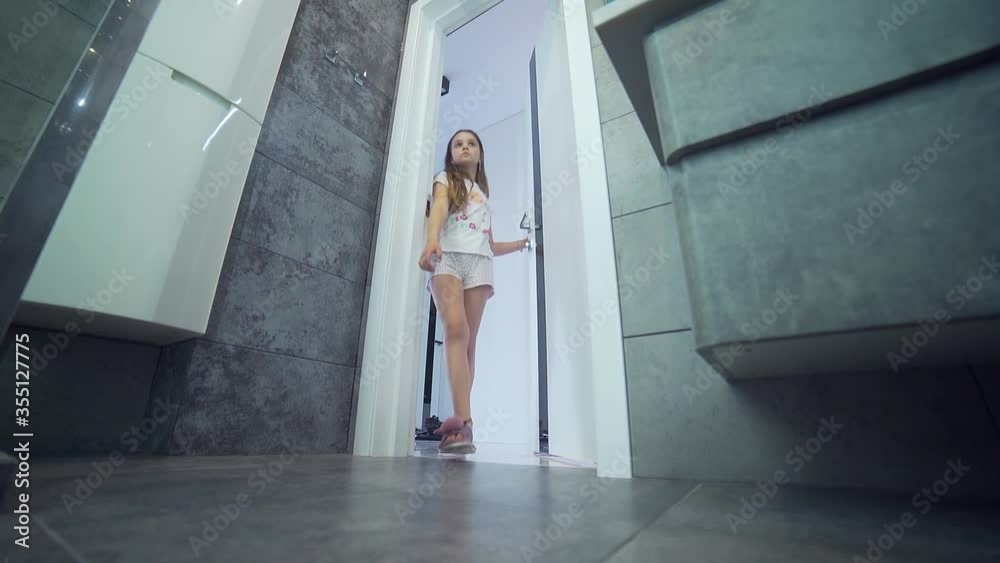 
little teen girl in pajamas opens the door and enters the bathroom. A pretty girl with long hair goes to wash in the morning. Slow motion