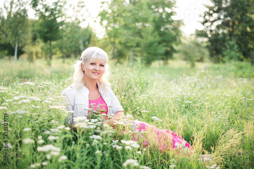 blonde girl is sitting in a meadow in the green grass
