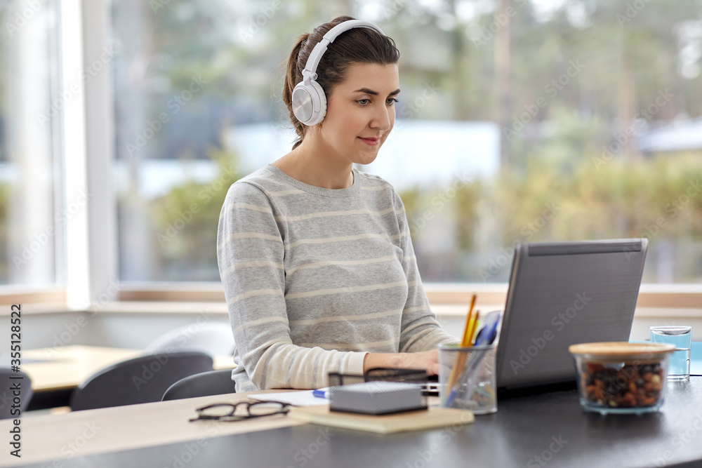 Obraz premium remote job, technology and people concept - happy smiling young woman in headphones with laptop computer working at home office