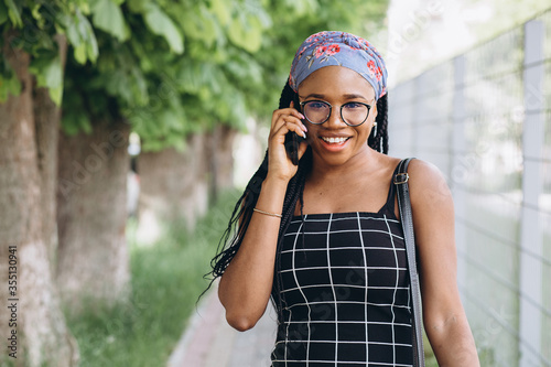 Pretty African American woman in a dress has fun outside and talks by phone