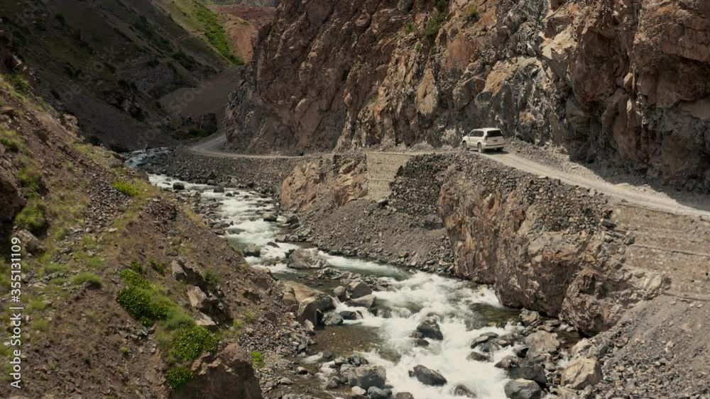 White SUV driving under a big overhanging rock, dangerous road by a wild river White SUV driving under a big overhanging rock, dangerous road by a wild river