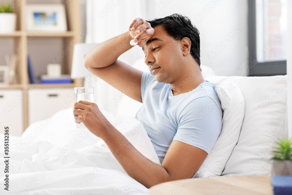 people, bedtime and rest concept - sick indian man lying in bed with medicine pill and glass of water at home people, bedtime and rest concept - sick indian man lying in bed with medicine pill and glass of water at home