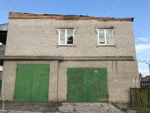 two-storey building, a white brick building, with a single-pitched roof with windows on the second floor and green metal garage gates on the first