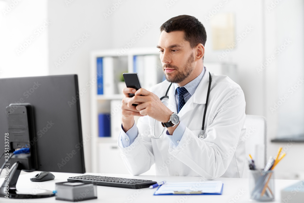 Obraz premium healthcare, medicine and people concept - male doctor with smartphone at hospital