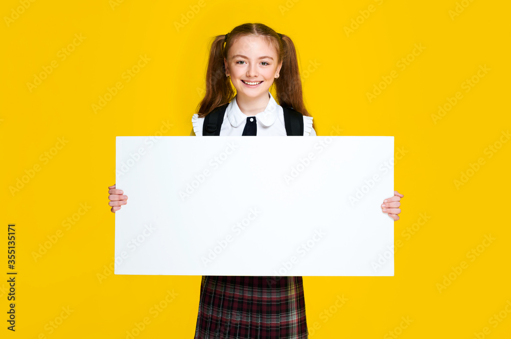 Schoolgirl student pupil holding big empty space white placard banner isolated yellow bright color background and smile Schoolgirl student pupil holding big empty space white placard banner isolated yellow bright color background and smile