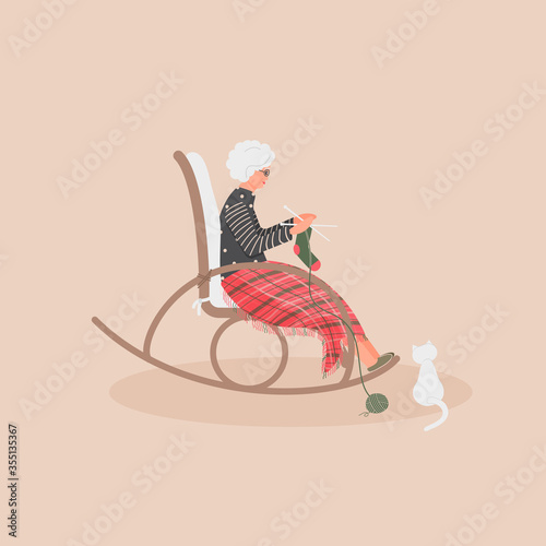 Elderly cute woman is sitting in a rocking chair.Old lady covered her feet with checked woollen plaid.Cartoon granny is knitting a sock in a comfortable rocker.White cat sit next.Vector illustration