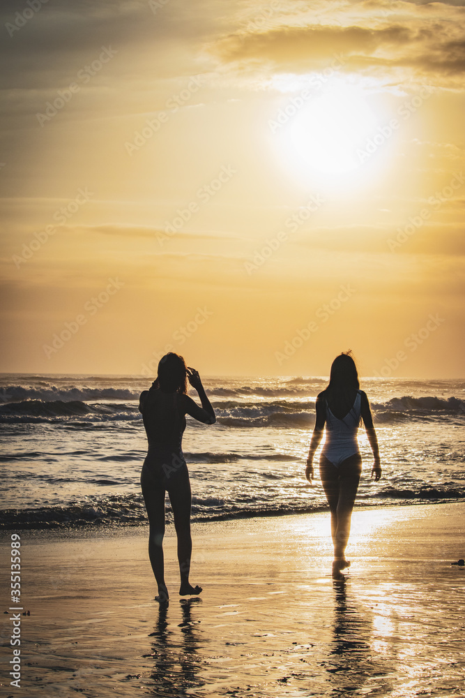 Fototapeta premium Two girls walking on the beach of Semyniak in Bali at sunset