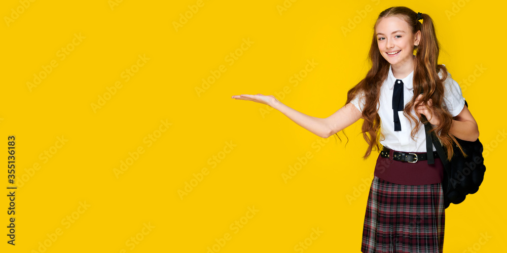 Schoolgirl in uniform and backpack holding something on isolated yellow background, copyspace, banner format Schoolgirl in uniform and backpack holding something on isolated yellow background, copyspace, banner format