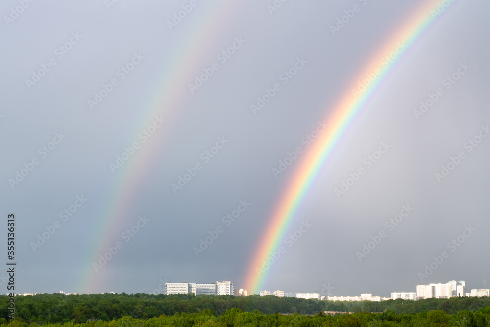 double rainbow over green city park and urban houses on horizon on spring day double rainbow over green city park and urban houses on horizon on spring day