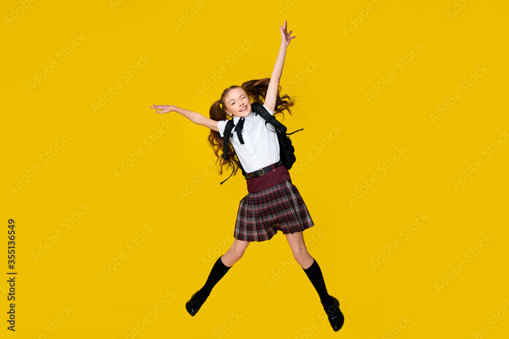 Full length photo of little funny crazy little lady schoolgirl pupil jump in uniform with backpack on vibrant yellow background, back to school, learning education concept Full length photo of little funny crazy little lady schoolgirl pupil jump in uniform with backpack on vibrant yellow background, back to school, learning education concept