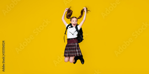 Fotografie Secondary school happy pupil jump in uniform with backpack on vibrant yellow bac