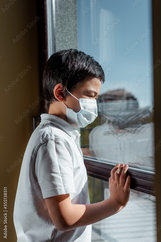 asian boy in medical mask looking through window on quarantine