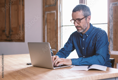 Good looking middle aged modern man having an online meeting on his laptop and tablet from home with his colleagues