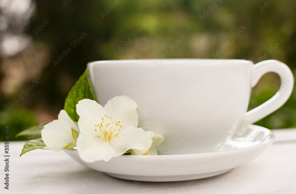 White cup of fragrant tea with a jasmine flower on a white wooden background. Place for text. Side view. White cup of fragrant tea with a jasmine flower on a white wooden background. Place for text. Side view.
