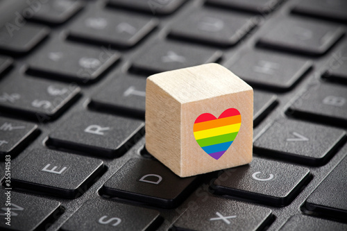 Wooden block with LGBT rainbow heart symbol of love on laptop keyboard.