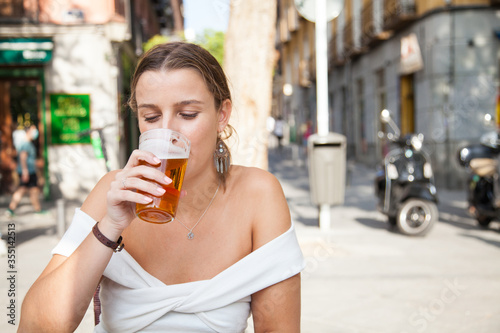 Chica rubia bebiendo cerveza en una terraza de un bar